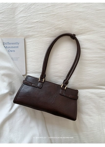 Top view of minimalist dark brown baguette bag on white fabric with an English book