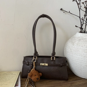 Detail of dark brown vintage handbag with gold clasp, long straps and bear charm