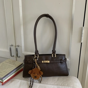 Close-up of vintage dark coffee shoulder bag with golden lock and plush bear charm
