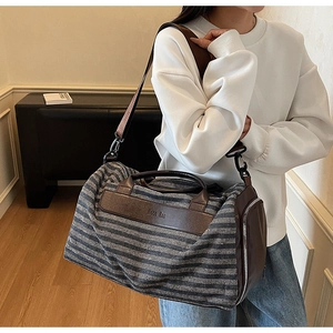 Détail du sac de voyage en toile rayée bleue avec poignées en cuir marron et logo