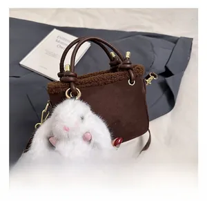 Détail du sac seau en daim marron foncé avec bordure en peluche et breloque lapin blanc