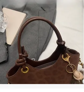 Borsa a secchiello marrone leopardata con manico a nodo e ciondolo su giacca grigia