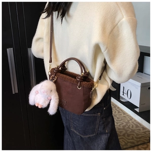 Dettaglio borsa a secchiello in camoscio marrone con bordo in shearling e ciondolo