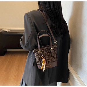 Vue détaillée du sac seau léopard avec base en cuir et accessoire de charme en perles