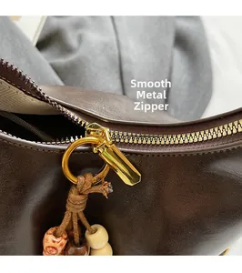 Detail of smooth golden metal zipper and decorative beaded tassel on dark brown bag