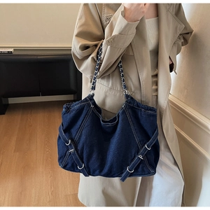 Detail of blue denim tote bag featuring silver chain straps and metallic buckle accents