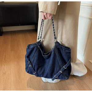 Detail of blue denim tote bag with silver chain handle and decorative side eyelet straps