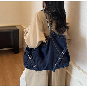 Detail of blue denim tote bag featuring adjustable buckled straps and chain shoulder strap