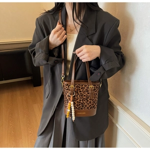 Détail du sac seau léopard élégant avec finitions en cuir marron et breloque en perles colorées
