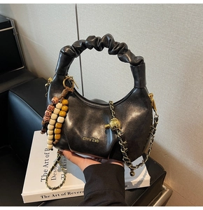 Detail of black pleated croissant bag with leather handle and colorful wooden beads