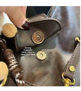 Detail view of the strong magnetic closure and plush charm on a large brown leather tote bag