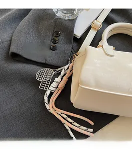 Detail of cream Boston bag with metallic tennis racket and woven rope pendants