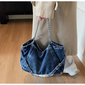 Detail of blue denim tote bag featuring silver chain strap and decorative side buckles