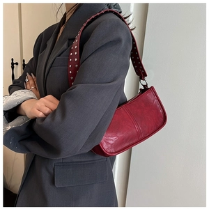 Detail of red baguette bag featuring decorative silver studs on the wide shoulder strap