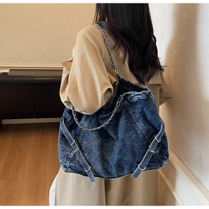 Detail of vintage washed denim tote bag with metal chain strap on khaki coat