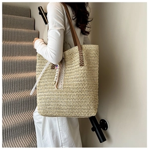 Detail view of woven straw tote bag with white lace, colorful beads and brown leather strap