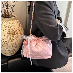 Close-up of pink quilted bucket bag with lace bow and gold chain strap on model