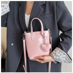 Detail of pink glossy mini tote bag with heart charm and crossbody strap on model