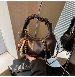 Detail of dark brown dumpling bag featuring pleated handle, chain strap, and bead tassel charm