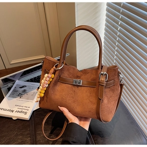 Détail du sac seau en daim marron foncé avec lanière en cuir et breloque en perles de bois