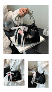 Detail of black quilted bucket bag featuring a large white lace bow and gold chain strap