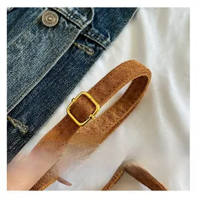 Close-up of brown suede shoulder strap with golden square buckle and matte texture