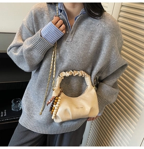 Detailed view of beige pleated crescent bag with wooden bead charm and metal chain strap