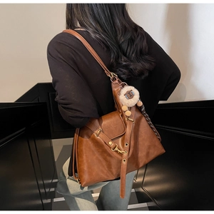 Detail of a brown leather tote bag with metallic buckles and a cute white sheep keychain