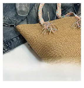 Detail of woven straw tote bag with pink blue and beige rope handle on denim background