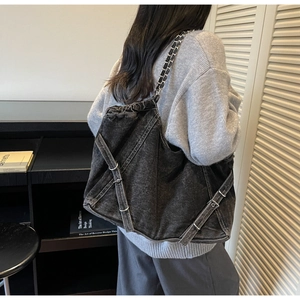 Detail of dark grey denim tote bag with metal chain strap and decorative buckle strap