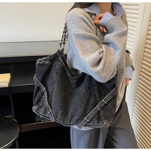 Detail of a large black denim tote bag featuring chain straps and a drawstring closure