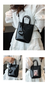 Detail of black glossy bucket bag featuring a heart pendant and rear transparent card slot