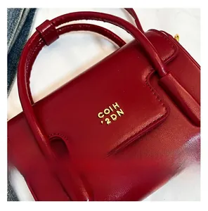 Gros plan sur le sac à main en cuir rouge avec logo métallique doré et texture grainée