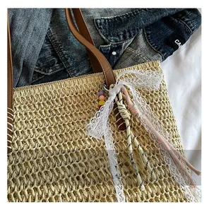 Detail showing natural woven straw texture with brown faux leather strap and lace bow