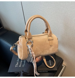 Close-up of beige suede Boston bag with smooth leather handles and elegant tassel detail