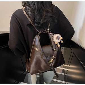 Detail of dark brown leather tote bag featuring a plush lamb charm and logo