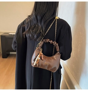 Detailed close-up of dark brown pleated leather dumpling bag with gold chain and wooden beads