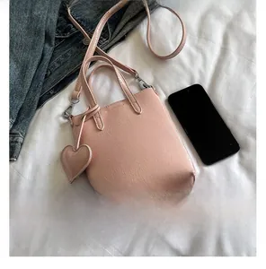 Detail of pink crinkled patent leather mini crossbody bag with heart charm and strap