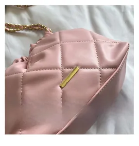 Detail of pink quilted leather bucket bag with gold chain strap and metal bar trim
