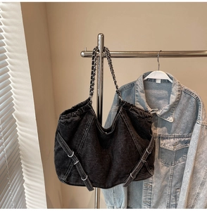 Detailed close-up of washed black denim tote bag with silver chain strap and white stitching