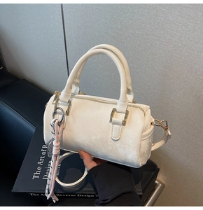 Detail view of pearlescent white Boston bag featuring gold hardware and woven charm