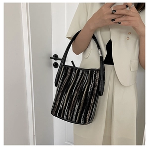 Detalle del bolso tipo cubo tejido con rayas marrón negro y asa de cuero fino