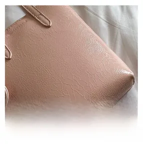 Detailed close-up showing the cracked texture and fine stitching on the pink crossbody bag