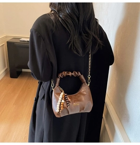Detail of a brown pleated handbag with golden chain strap and beaded charm ornament