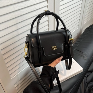 Sac boîte noir minimaliste avec détails dorés et bandoulière réglable dans un décor épuré