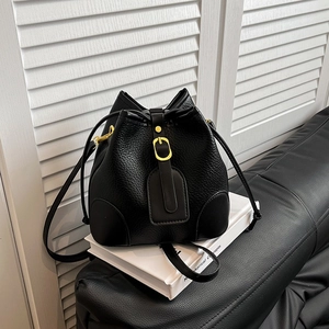 Chic black lychee grain leather bucket bag with gold buckle on a minimalist background