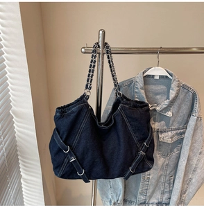 Detail of blue denim tote bag with metal chain strap and decorative silver ring buckles
