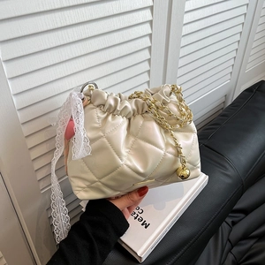 Chic beige quilted chain bucket bag with decorative gold ball and lace bow detail