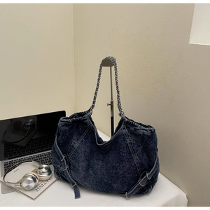 Detail of blue denim tote bag with metal chain strap and decorative side buckle accents