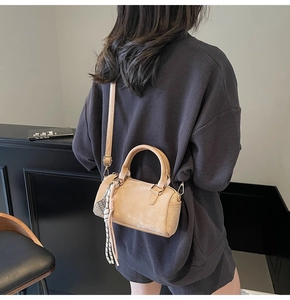 Side view of beige Boston bag with tassel charm worn as a crossbody on grey set